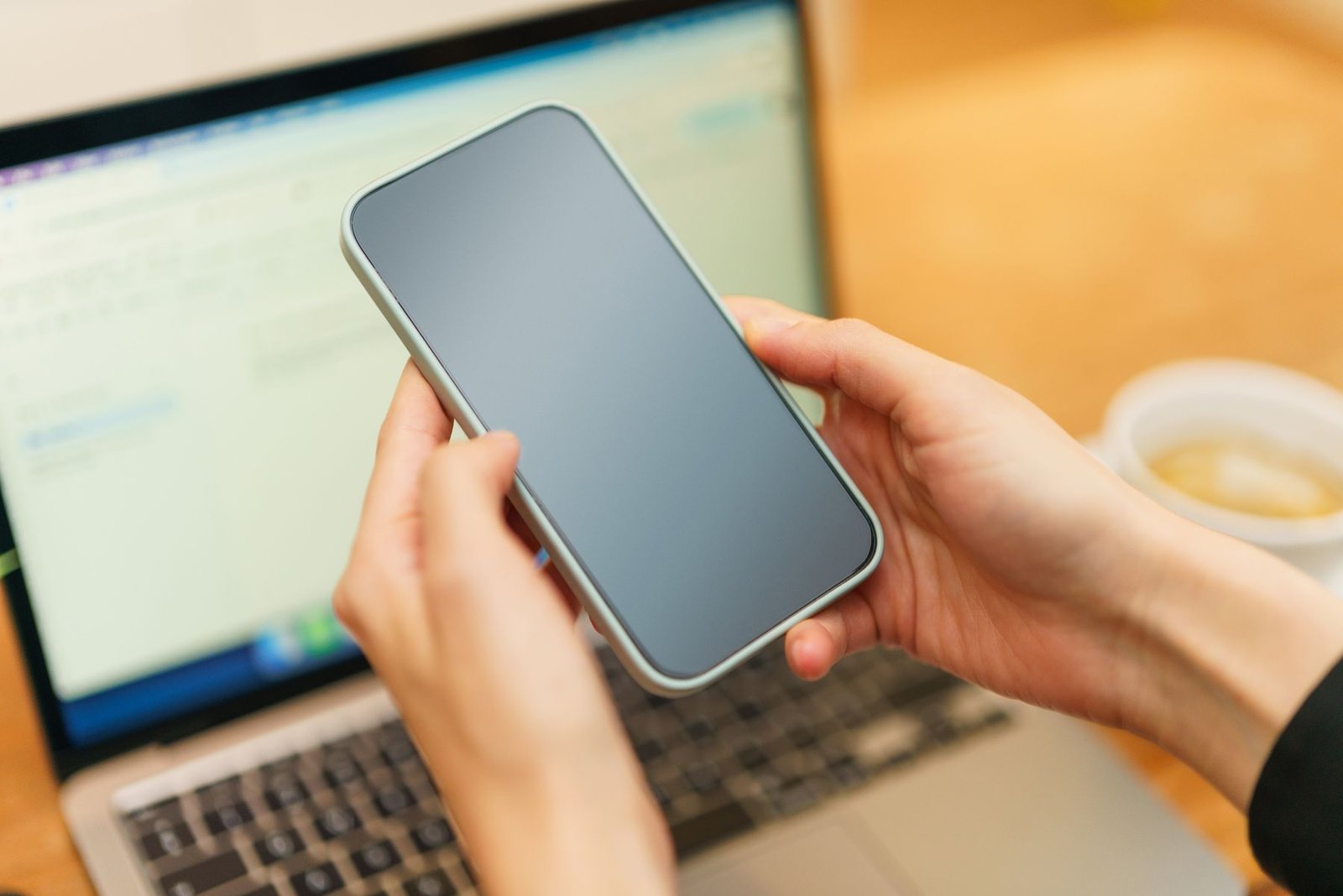 Hands holding a phone above a laptop while searching
