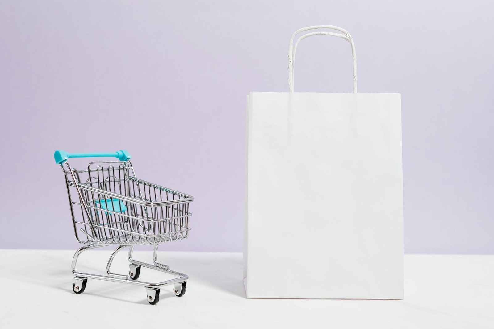 A miniature shopping cart next to a white paper shopping bag