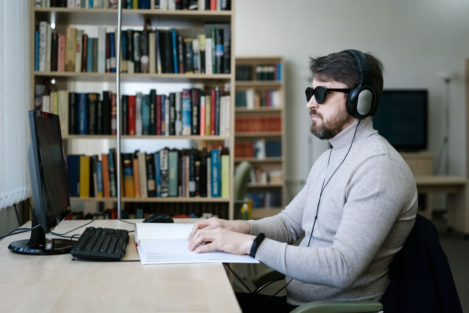 A man using a computer with headphones and a screen reader