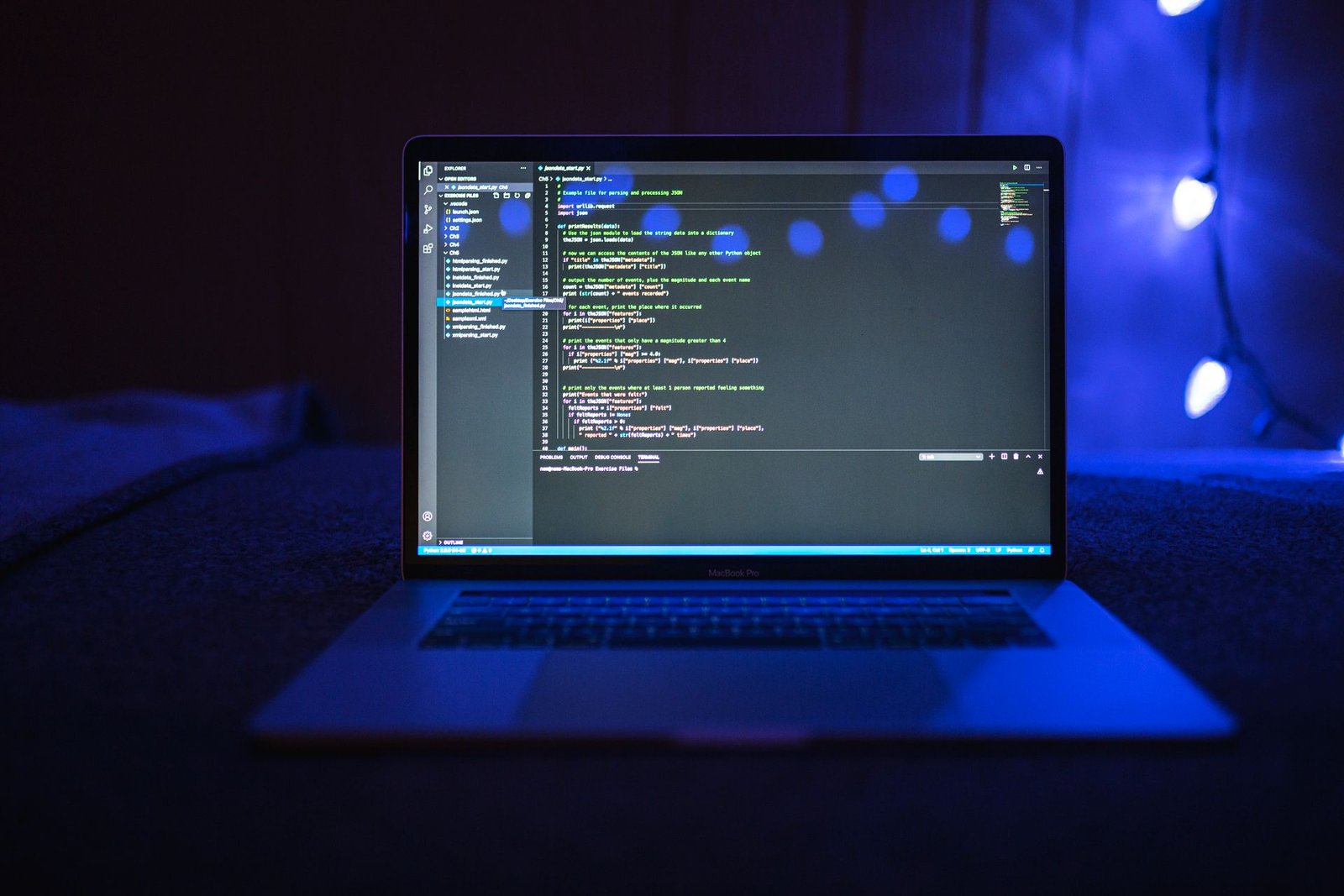 A laptop showing code on a desk in a dark room lit with blue light