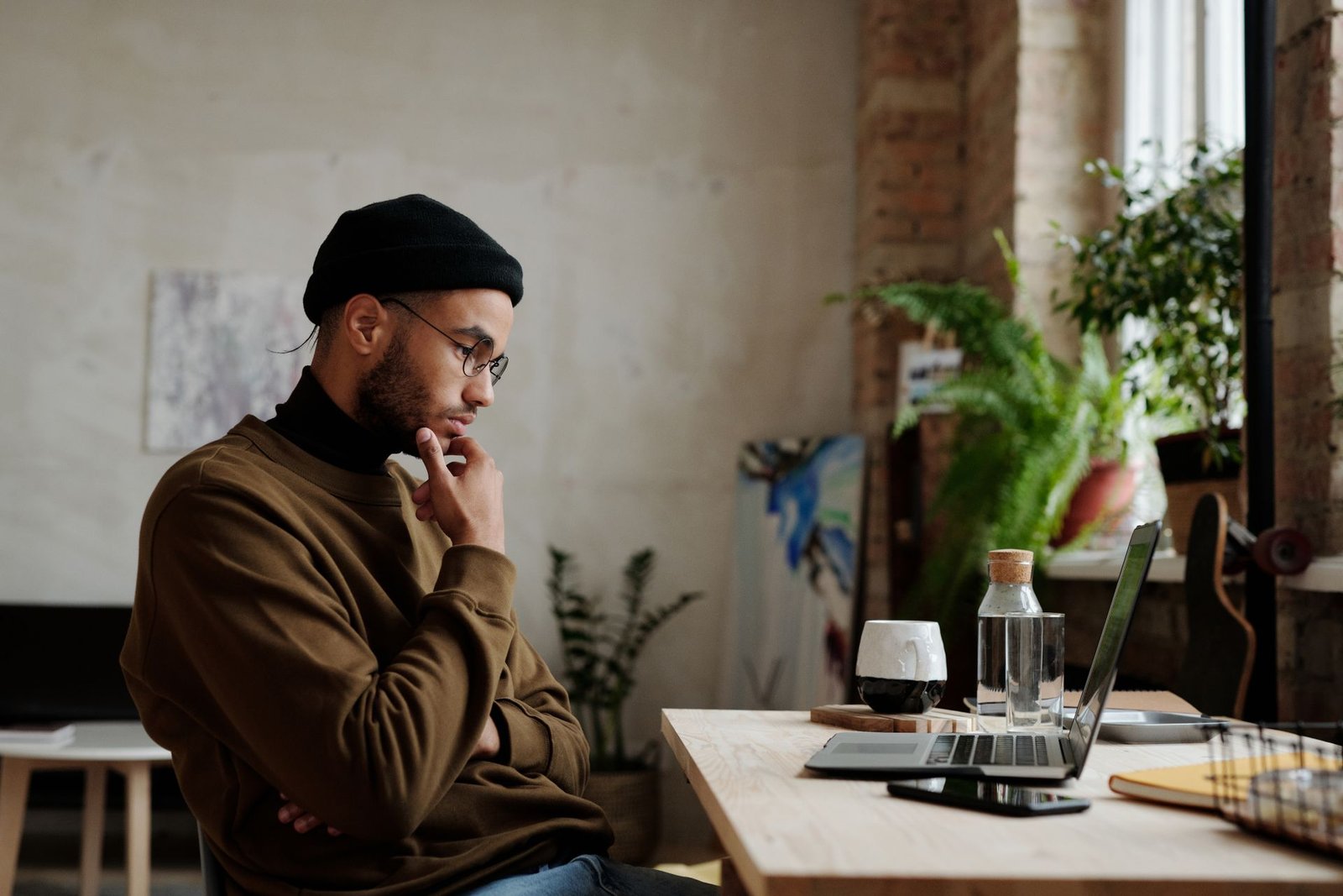 A man at a desk with his hand on his chin, thinking while looking at his laptop