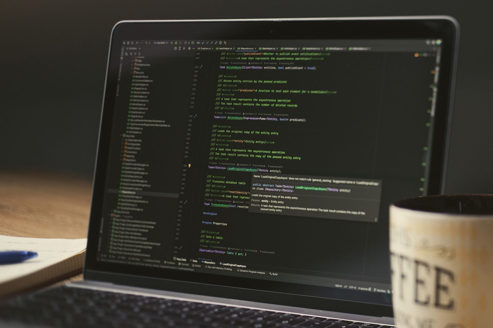 A laptop showing code beside a coffee mug on a dark desk