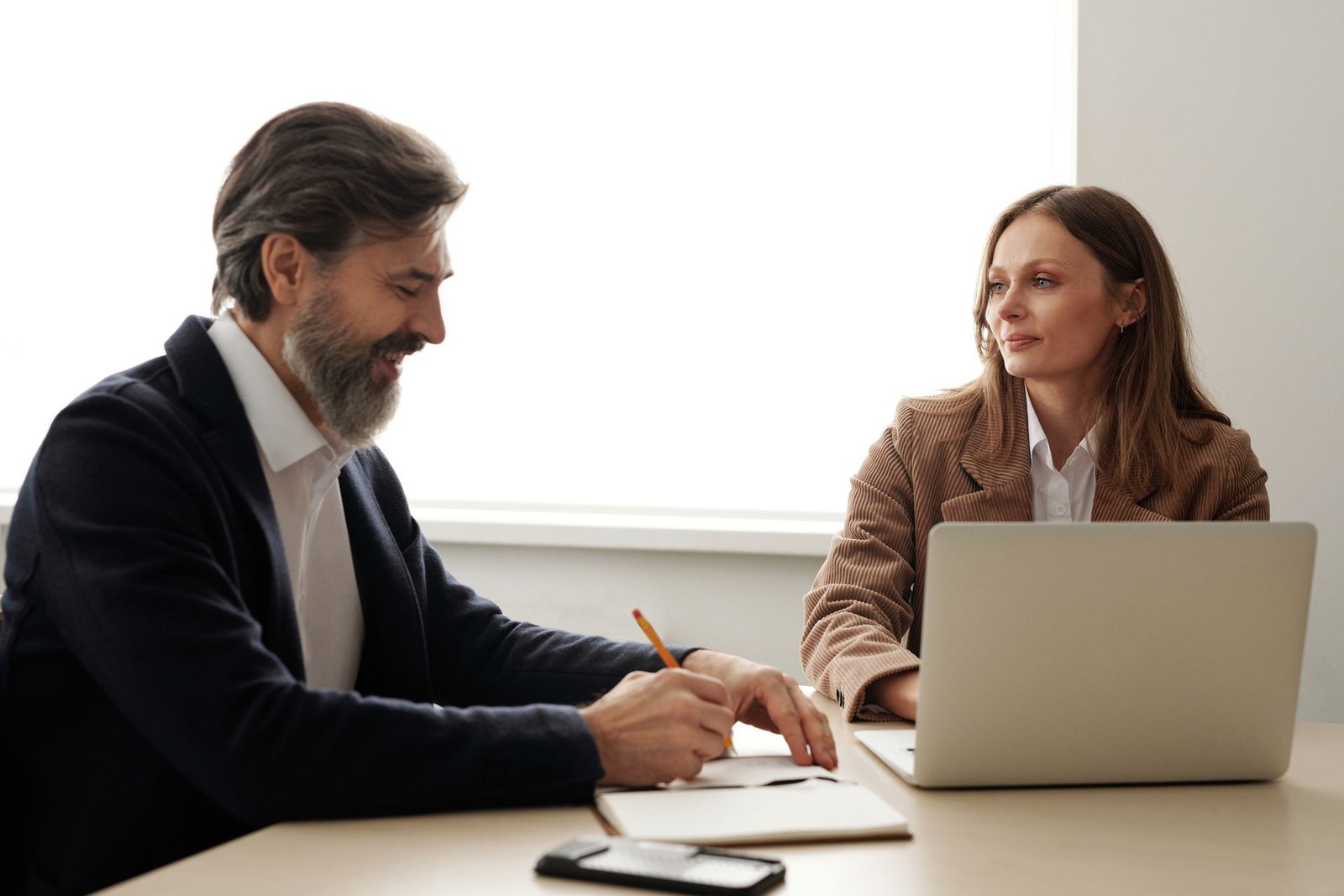 An agency owner and a client talking across a table with a laptop and notes