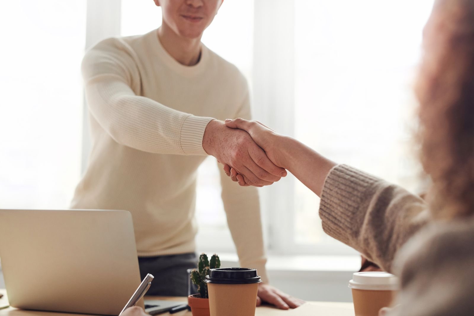 Agency owner shaking hands with a partner at a laptop